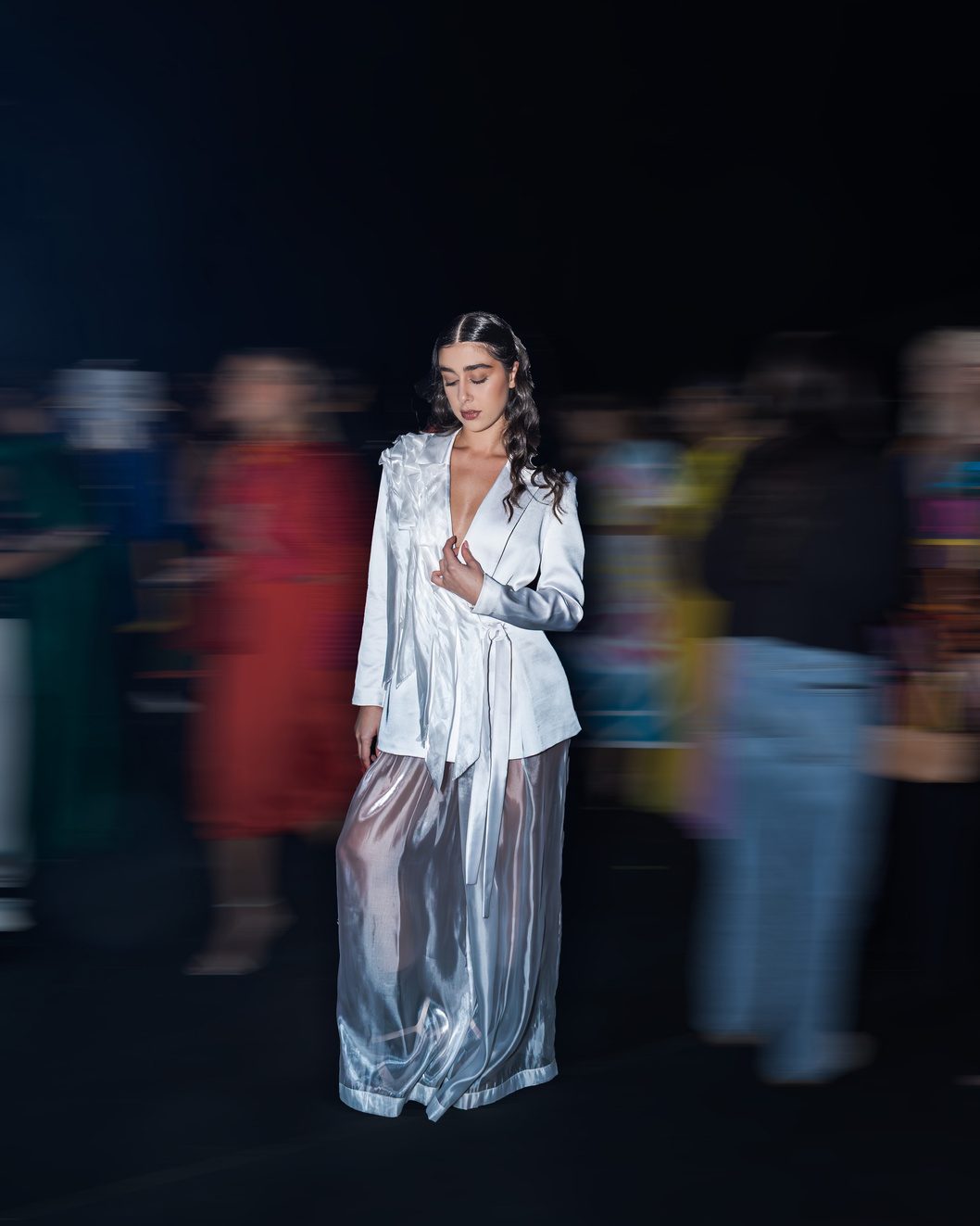 Model in white suit with motion-blurred crowd backstage